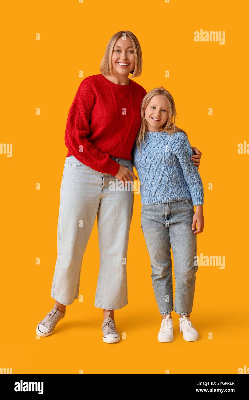 Donna felice e sua figlia carina in maglioni eleganti su sfondo giallo Foto Stock