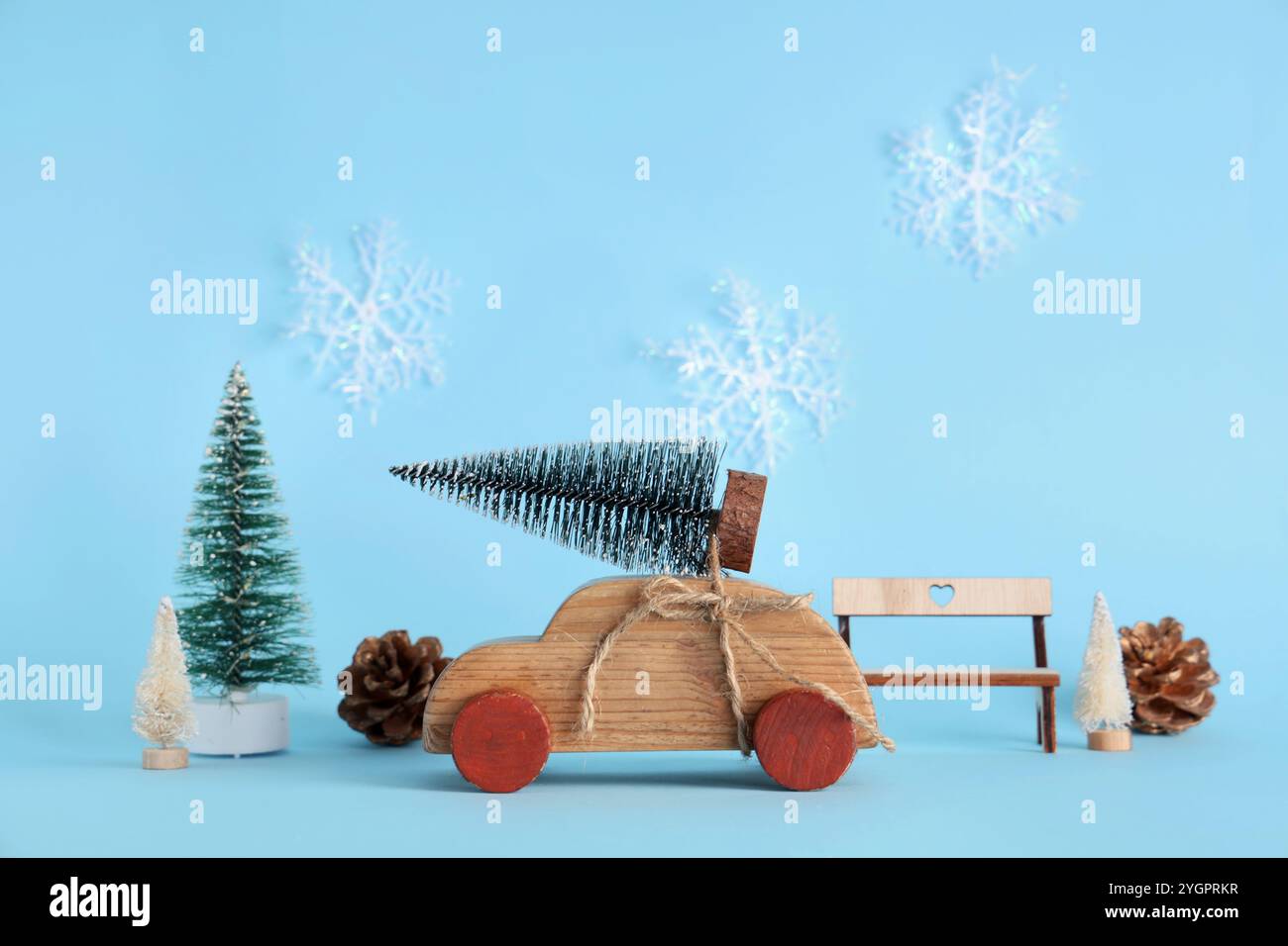 Macchinina di legno giocattolo con piccoli alberi di Natale, coni di pino e panca su sfondo blu Foto Stock
