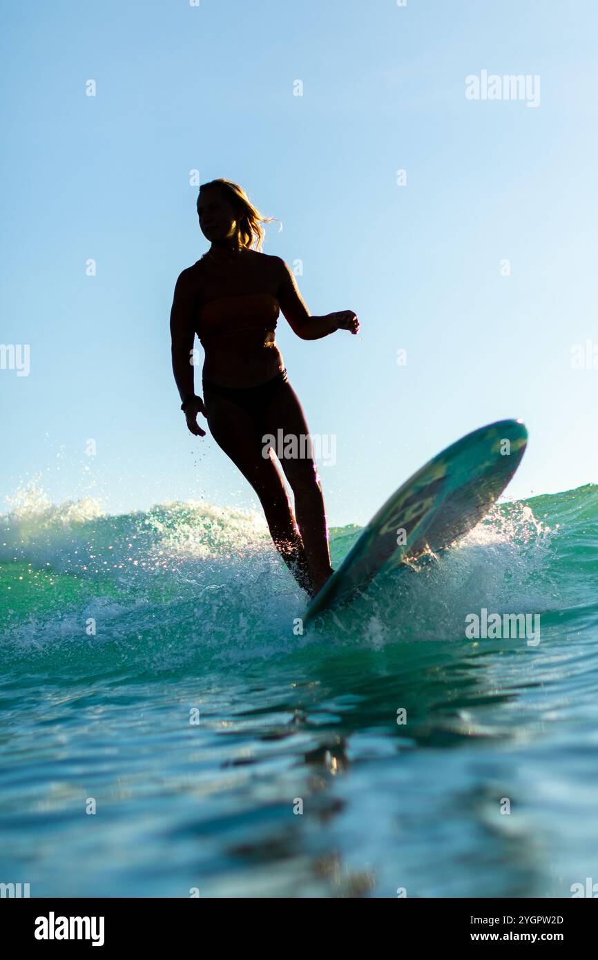 Il surfista cavalca con grazia un'onda a Waikiki, retroilluminata dal sole. Foto Stock