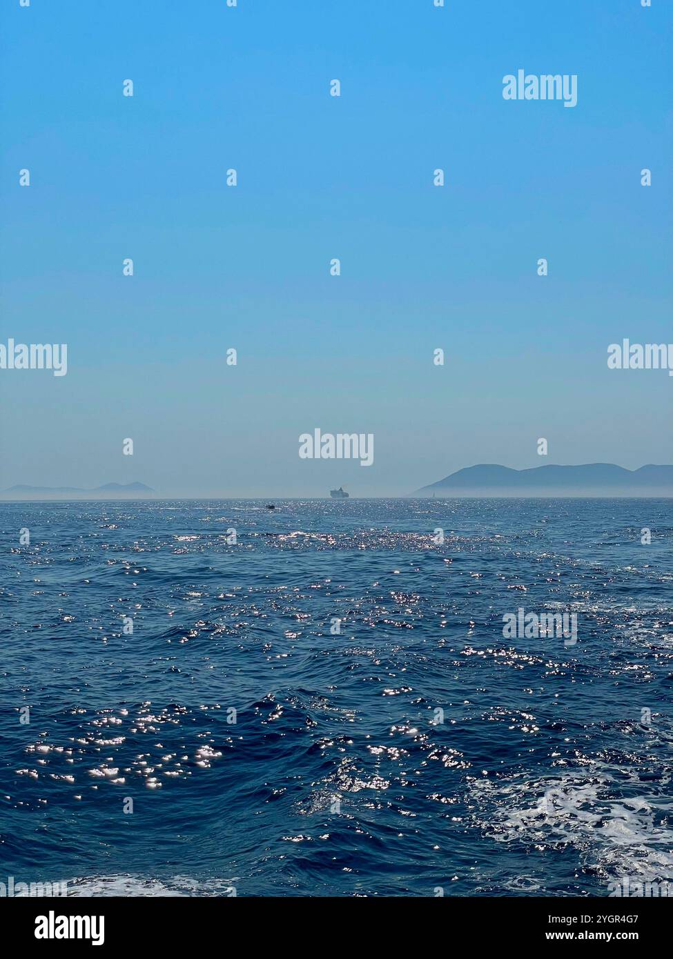 Le acque illuminate dal sole catturano Corfù, Grecia, durante un viaggio estivo del 2023. Una barca solitaria si allontana pacificamente, incorniciata da una terra lontana e da un blu senza fine. - Immagine stock catturata con smartphone