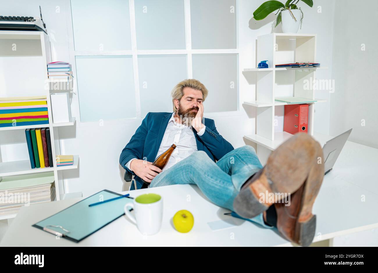 Un giovane dipendente d'affari che beve in ufficio alla scrivania. Triste stressato abuso alcolico ragazzo ottenere ubriaco sentire solo disperato circa la dipendenza. Foto Stock