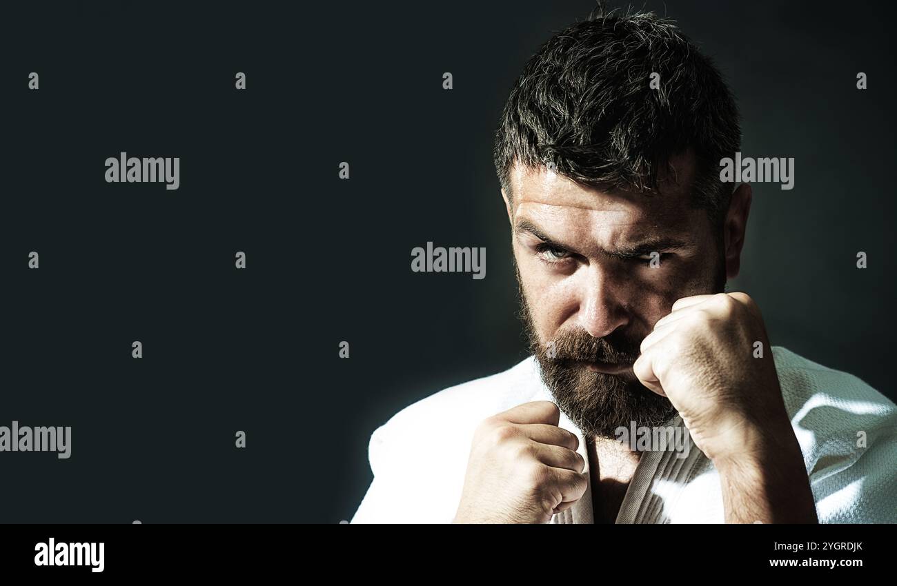 Uomo di karate con pugni clenati pronto per l'allenamento di karate. Serio uomo di karate barbuto in kimono bianco. Forte uomo di karate in posizione di combattimento preparando f Foto Stock