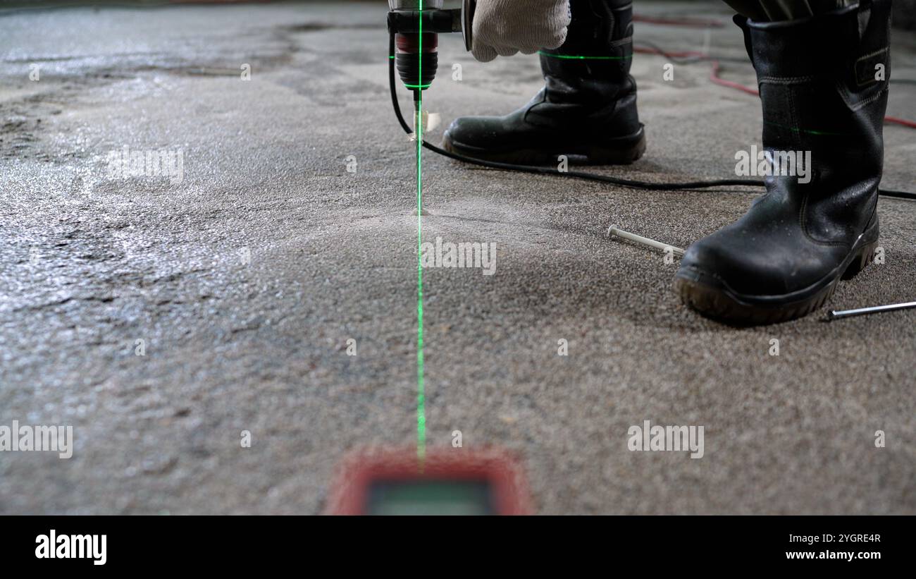 Foratura e installazione di perni nel pavimento. Un uomo esegue un foro nel pavimento con un martello per livellare il pavimento al laser. Un lavoratore pratica un plasti Foto Stock