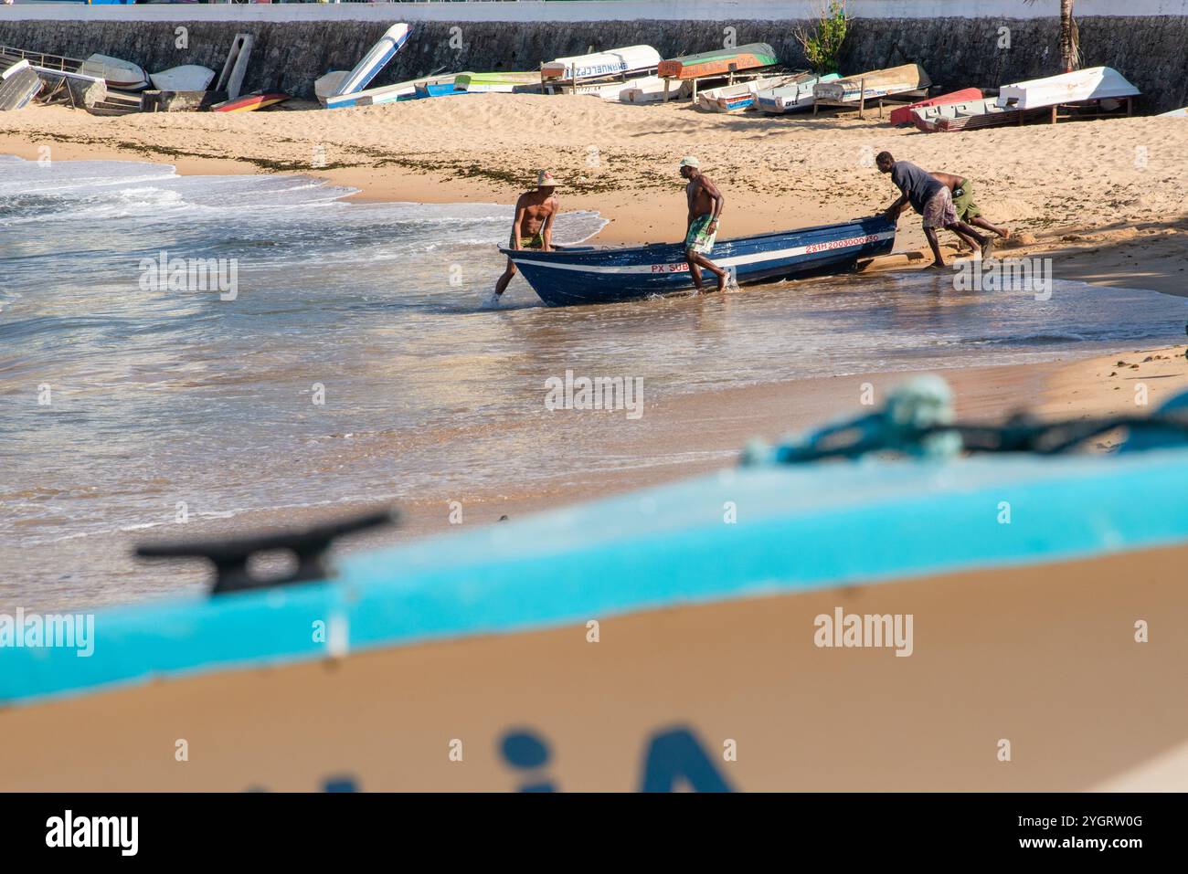 Si vedono pescatori che spingono una barca da pesca in mare sulla spiaggia di Rio Vermelho. Salvador, Bahia. Foto Stock