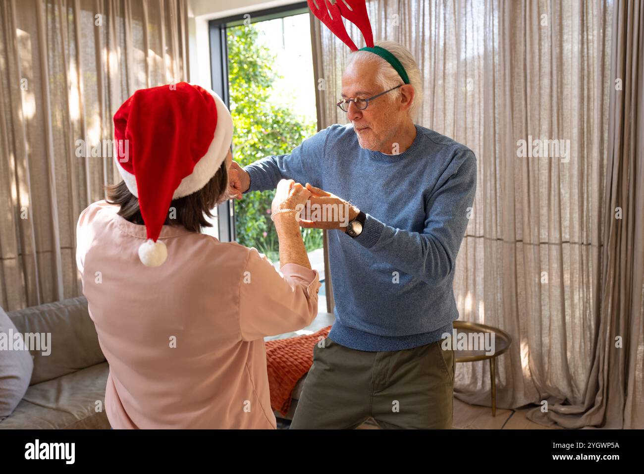 Coppia senior che balla con gioia a casa indossando cappelli natalizi Foto Stock