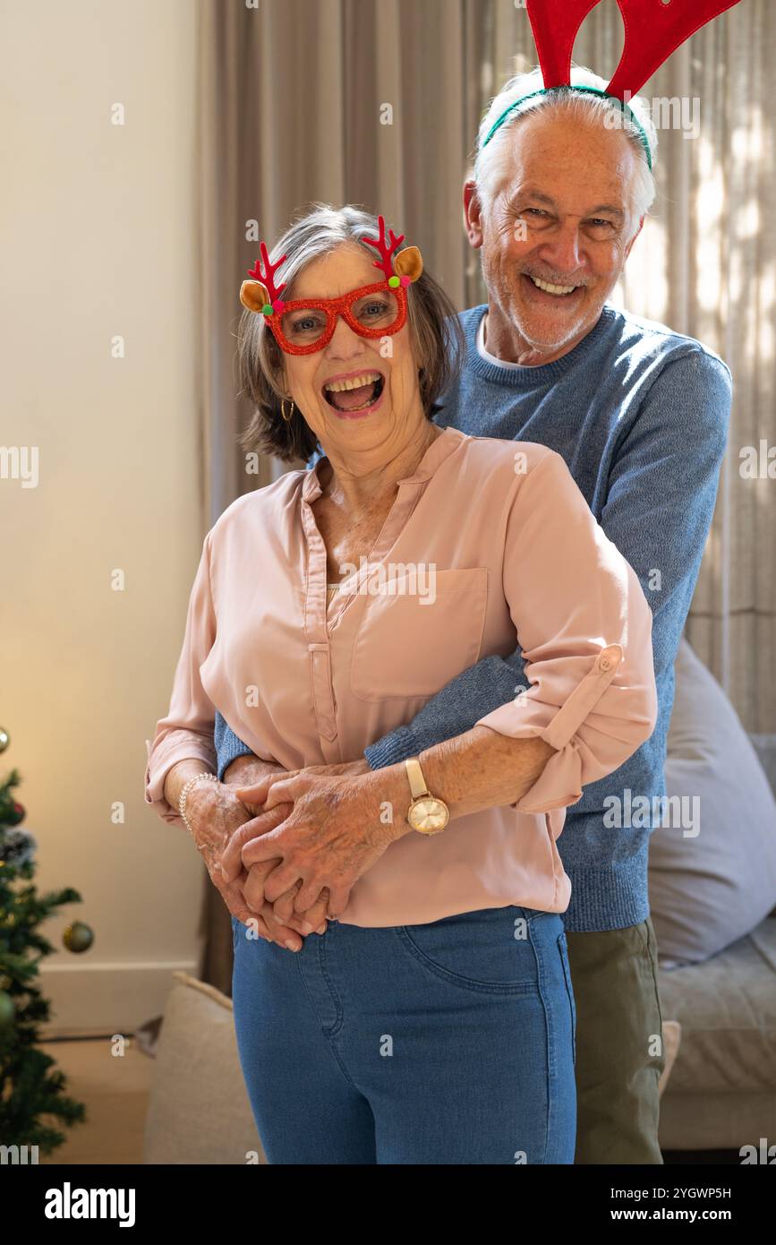 Gioiosa coppia senior che indossa corna di renna per celebrare il Natale a casa Foto Stock