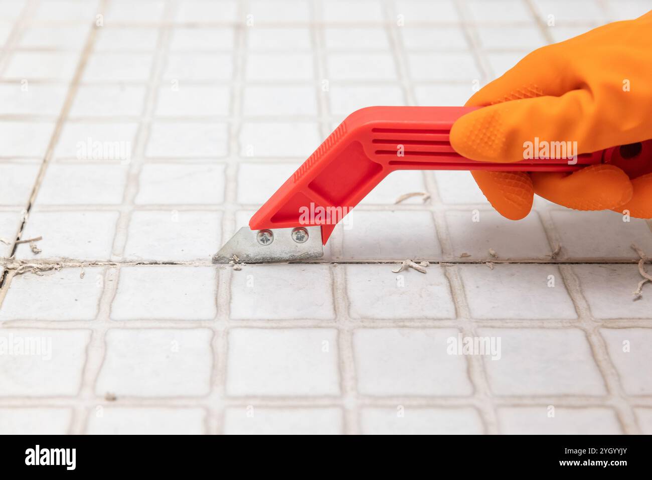 La governante rimuove la vecchia Malta dalle piastrelle del bagno. Rastrellare le piastrelle di Malta per riinstradare. Foto Stock