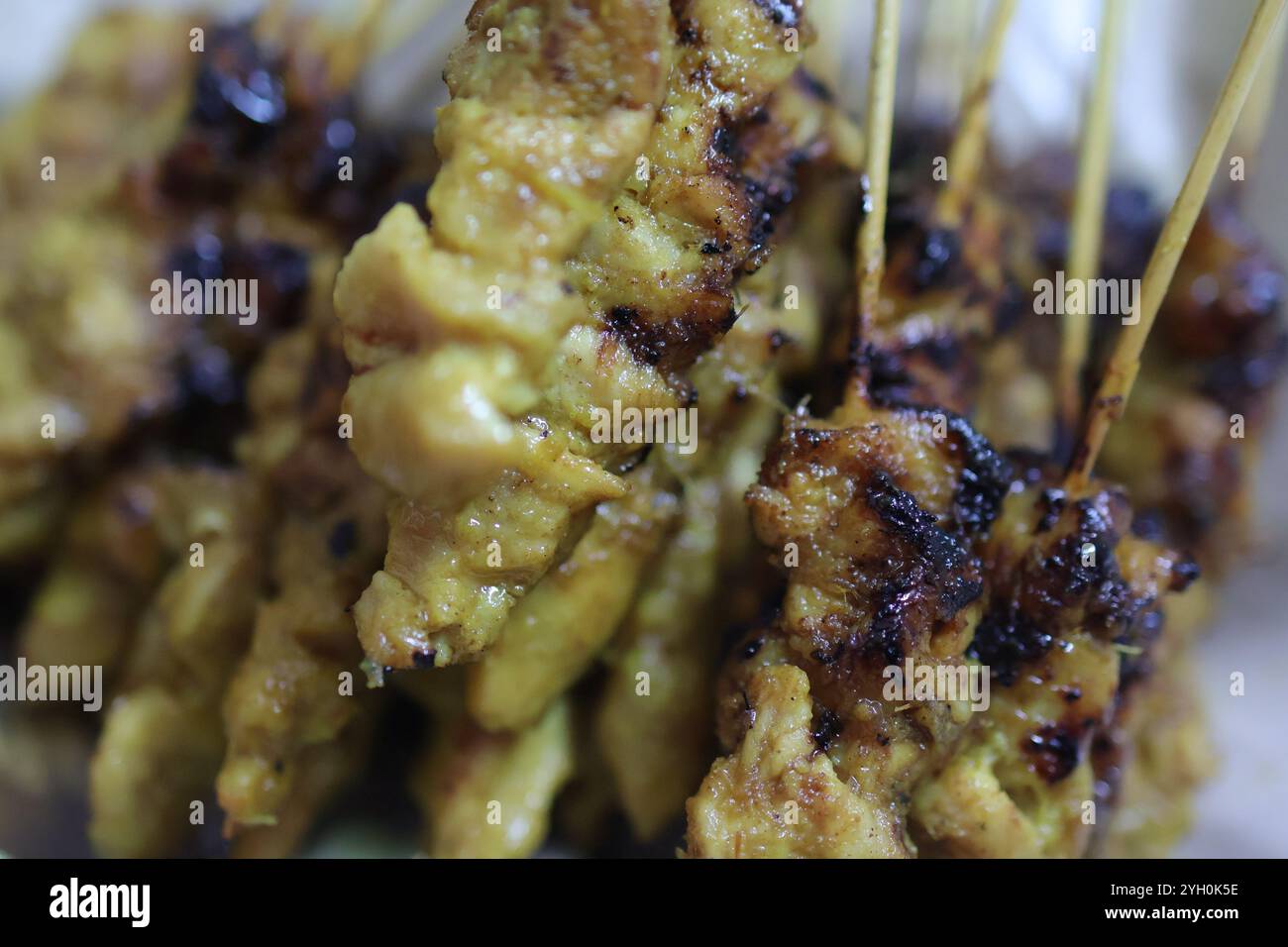 Succulento primo piano di satay di pollo grigliato su bastoncini di bambù, con bordi carbonizzati e ricca marinata. Foto Stock