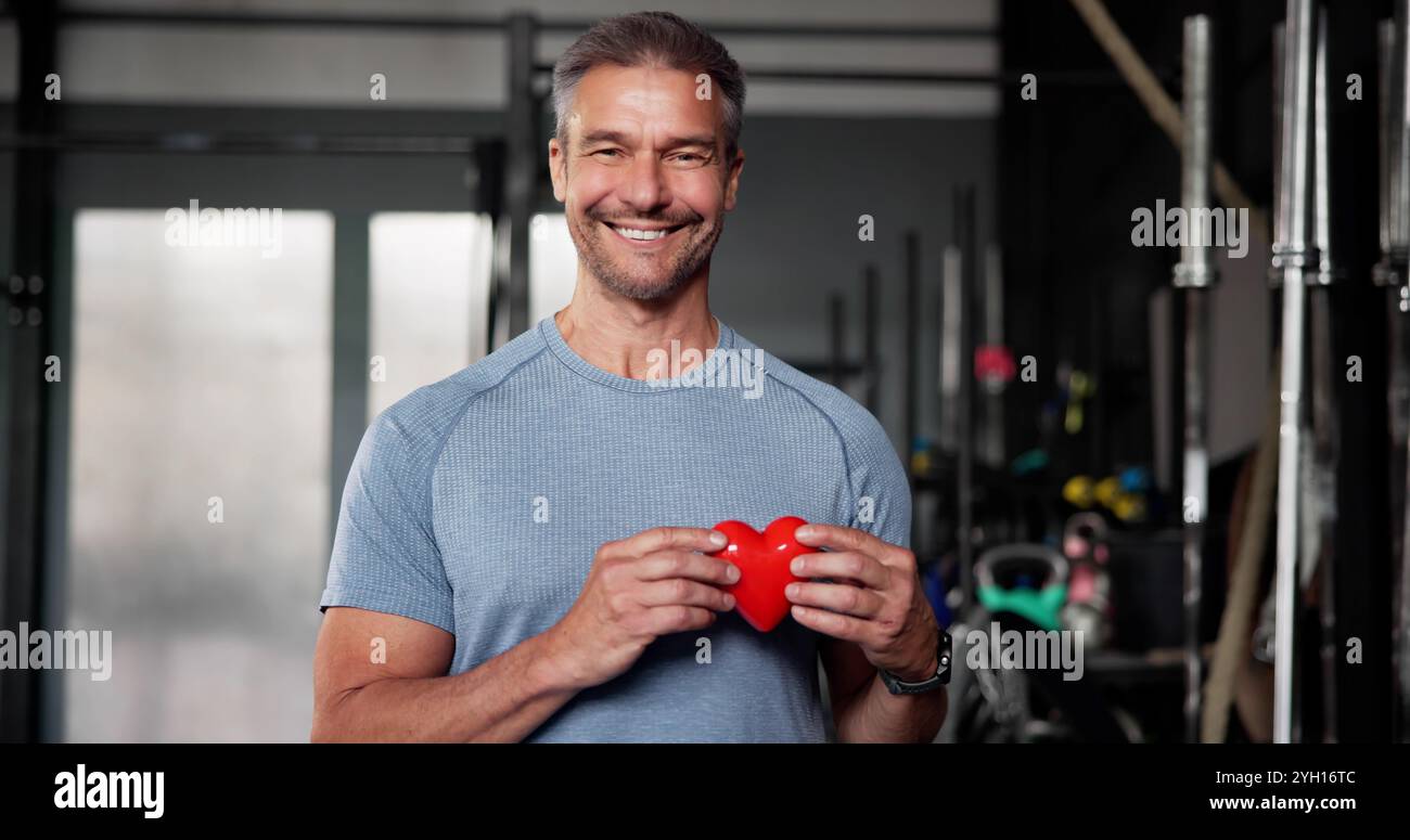 Uomo che tiene la forma del cuore in palestra. Amore per il fitness Foto Stock