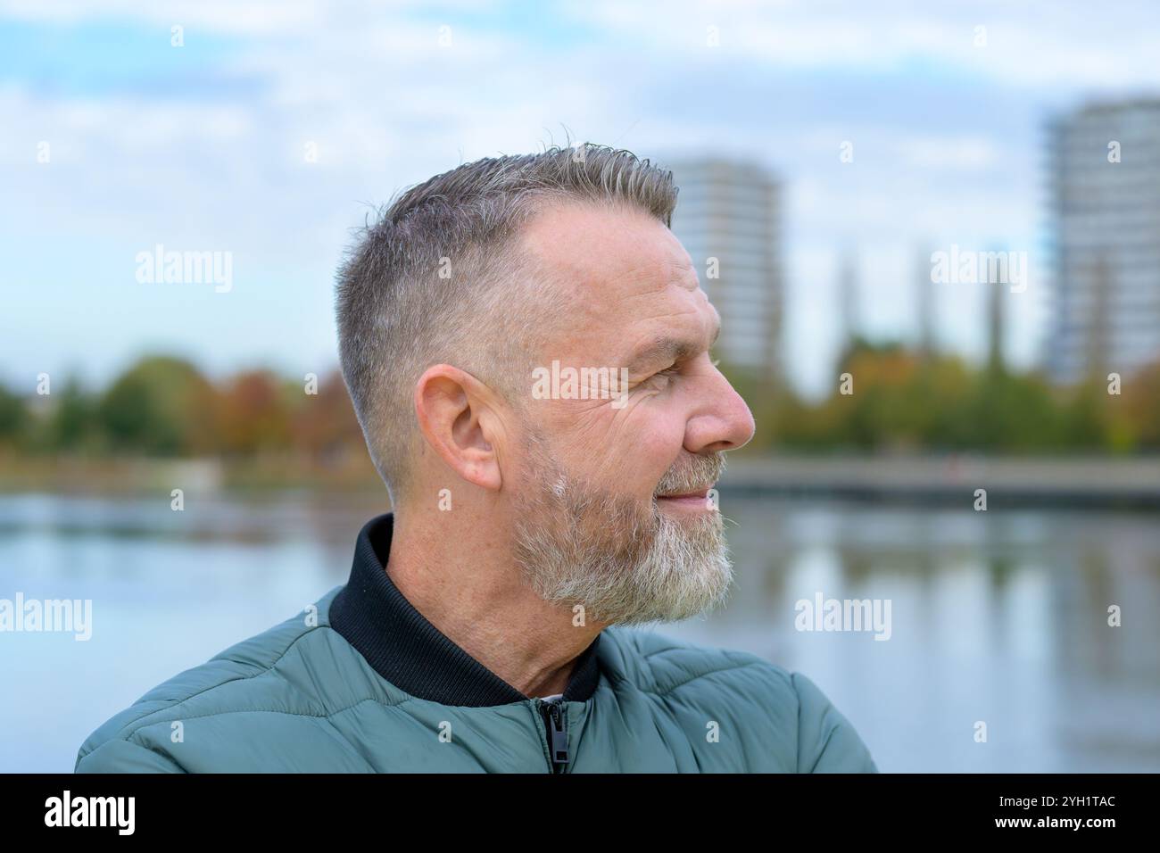 Profilo laterale di un uomo maturo con barba grigia, che guarda a destra con un sottile sorriso. Foto Stock