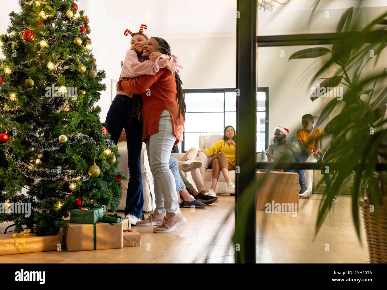 Famiglia multirazziale che celebra il Natale a casa, abbraccia vicino a un albero decorato, si sente gioiosa Foto Stock