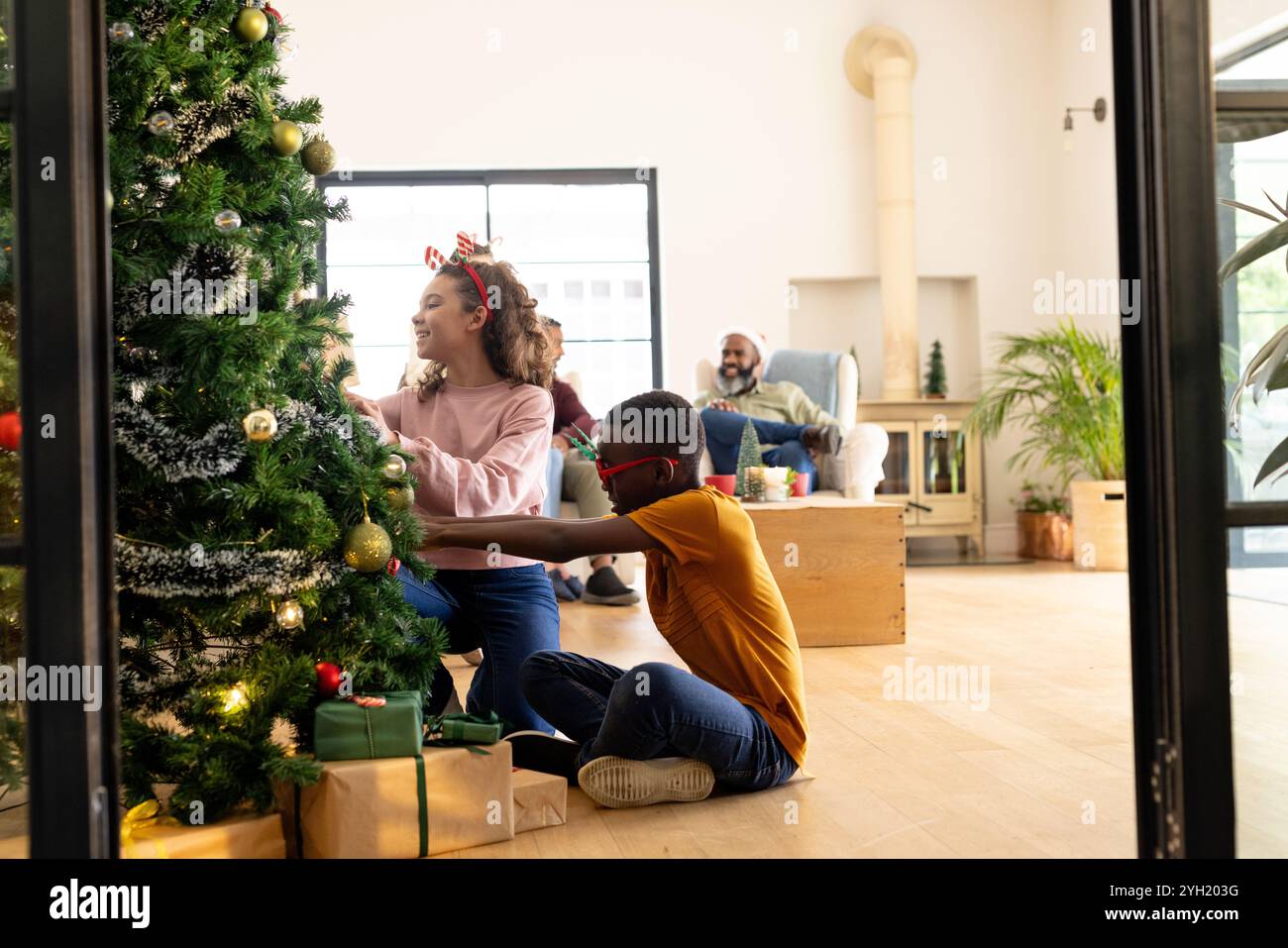 Famiglia multirazziale che decora l'albero di Natale insieme a casa, godendo momenti di festa Foto Stock