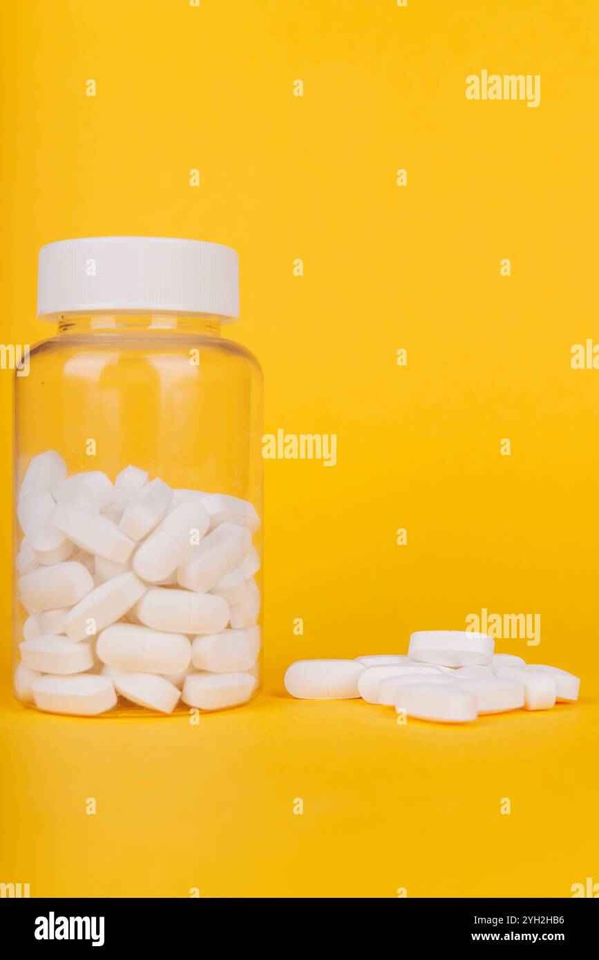 Bottiglia di pillola trasparente con compresse bianche su giallo, evidenziando l'essenziale della salute e del benessere nella medicina moderna Foto Stock