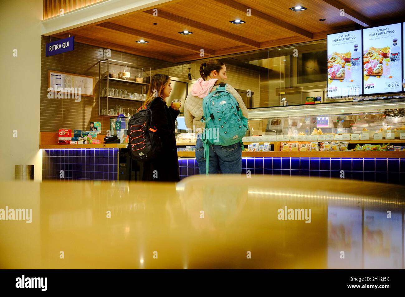 Traversetolo, Parma, Itally - 6 novembre 2024 due studentesse con zaini che ordinano cibo e bevande presso un banco di mensa universitaria Foto Stock