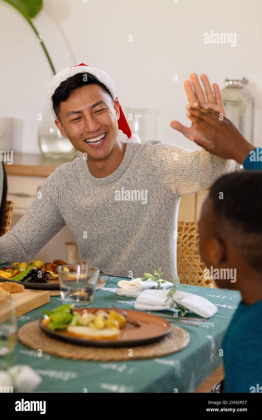 Festeggiamo il Natale, uomo gioioso con il cappello di Babbo Natale che si esibisce a cena festiva, a casa Foto Stock