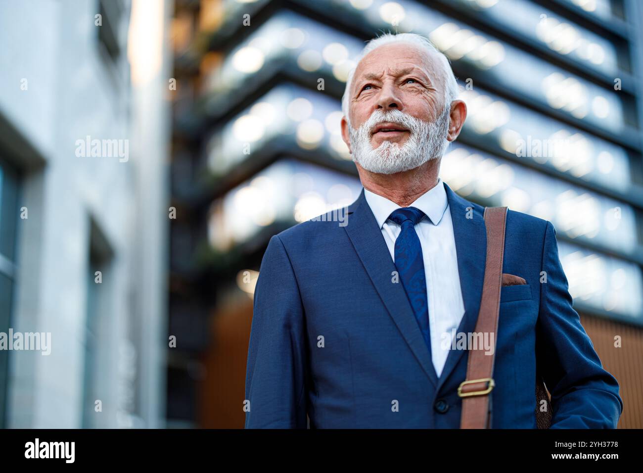 Ritratto di un uomo d'affari con la barba con la borsa per laptop che guarda lontano mentre si trova fuori dall'ufficio Foto Stock