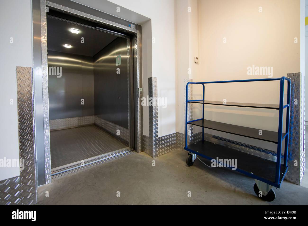 Ascensore aperto accanto a un carrello blu in un moderno deposito. Foto Stock