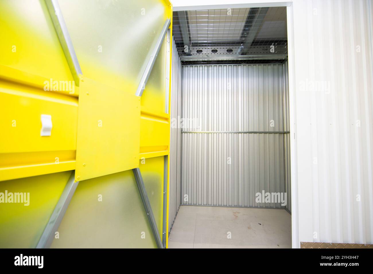 Aprire lo sportello giallo che rivela un'unità di stoccaggio vuota con pareti metalliche all'interno di una struttura. Foto Stock