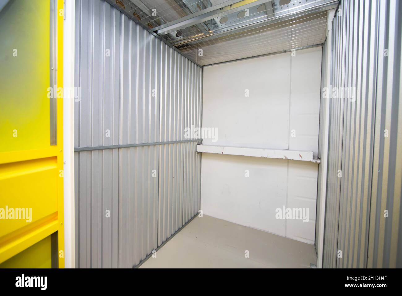 Aprire lo sportello giallo che rivela un'unità di stoccaggio vuota con pareti metalliche all'interno di una struttura. Foto Stock