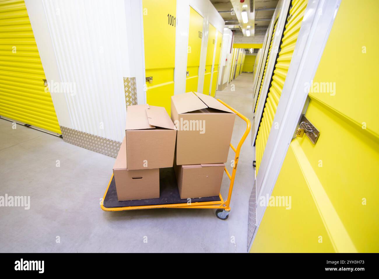 Carrello caricato con scatole di cartone in un luminoso corridoio di stoccaggio autonomo. Foto Stock