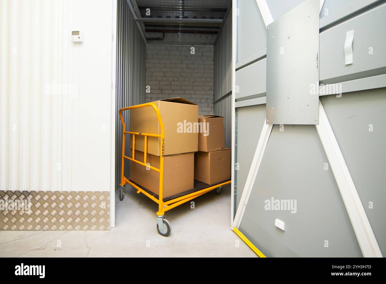 Carrello caricato con scatole di cartone in un luminoso corridoio di stoccaggio autonomo. Foto Stock