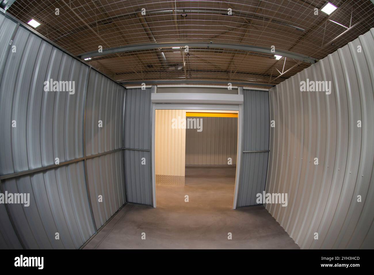Interno di un vano portaoggetti vuoto con pareti metalliche con vista su una porta arrotolabile gialla. Foto Stock