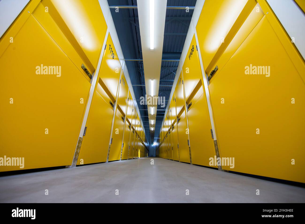 Corridoio simmetrico in un deposito con porte gialle luminose e illuminazione a soffitto. Foto Stock