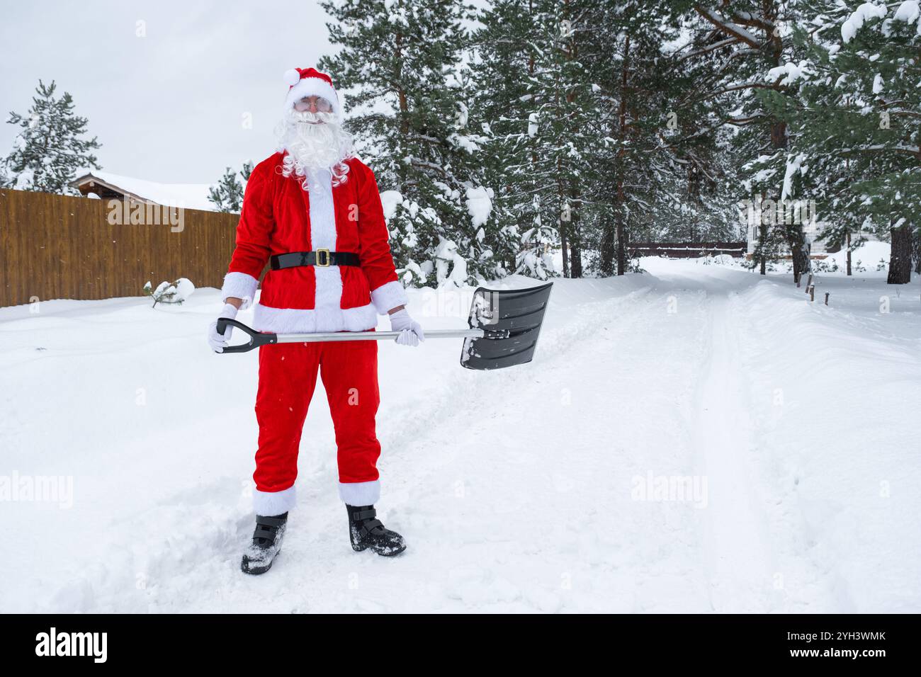 Babbo Natale pulisce la neve con la pala in inverno all'aperto dopo una nevicata. Pulire le strade del villaggio, pulire il passaggio per le auto, difficile Foto Stock