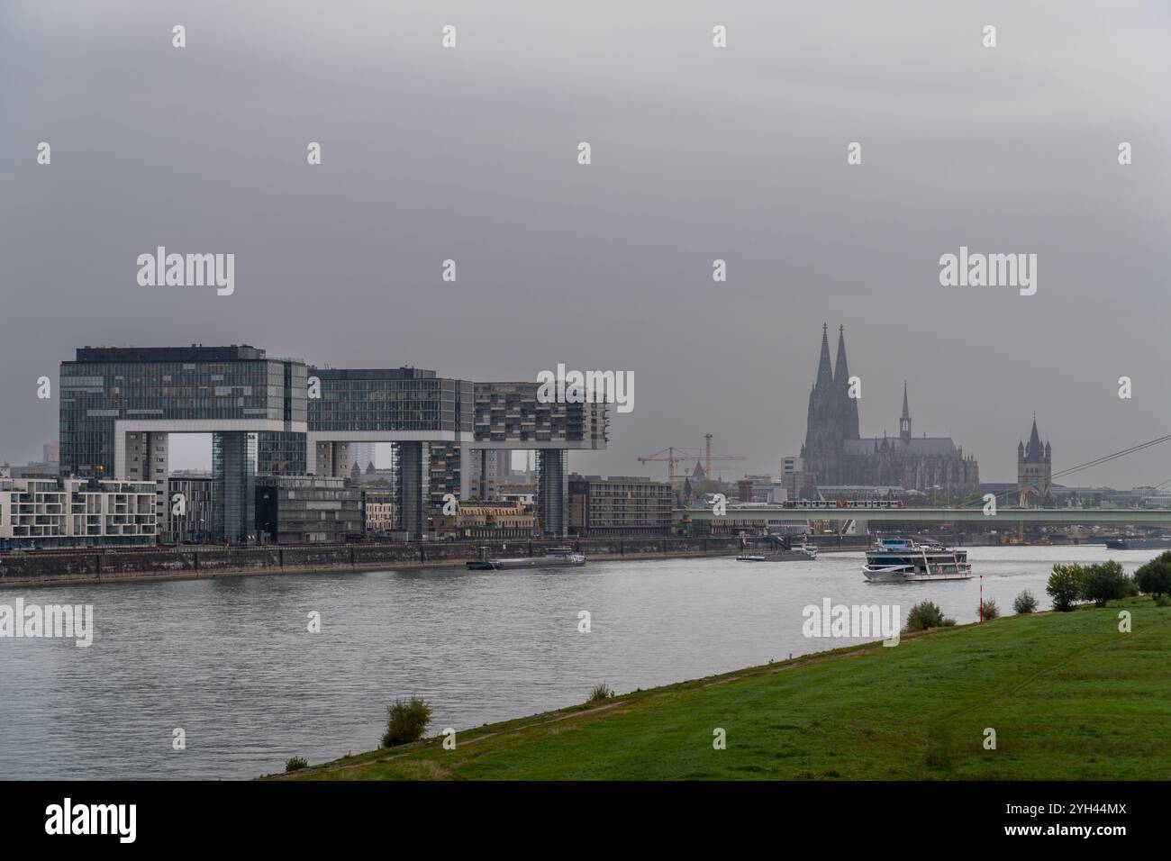 Un moderno paesaggio urbano caratterizzato da tre edifici unici a forma di gru lungo il fiume, con un ponte di fronte che trasporta un tram. Vista della Cattedrale di Colonia Foto Stock
