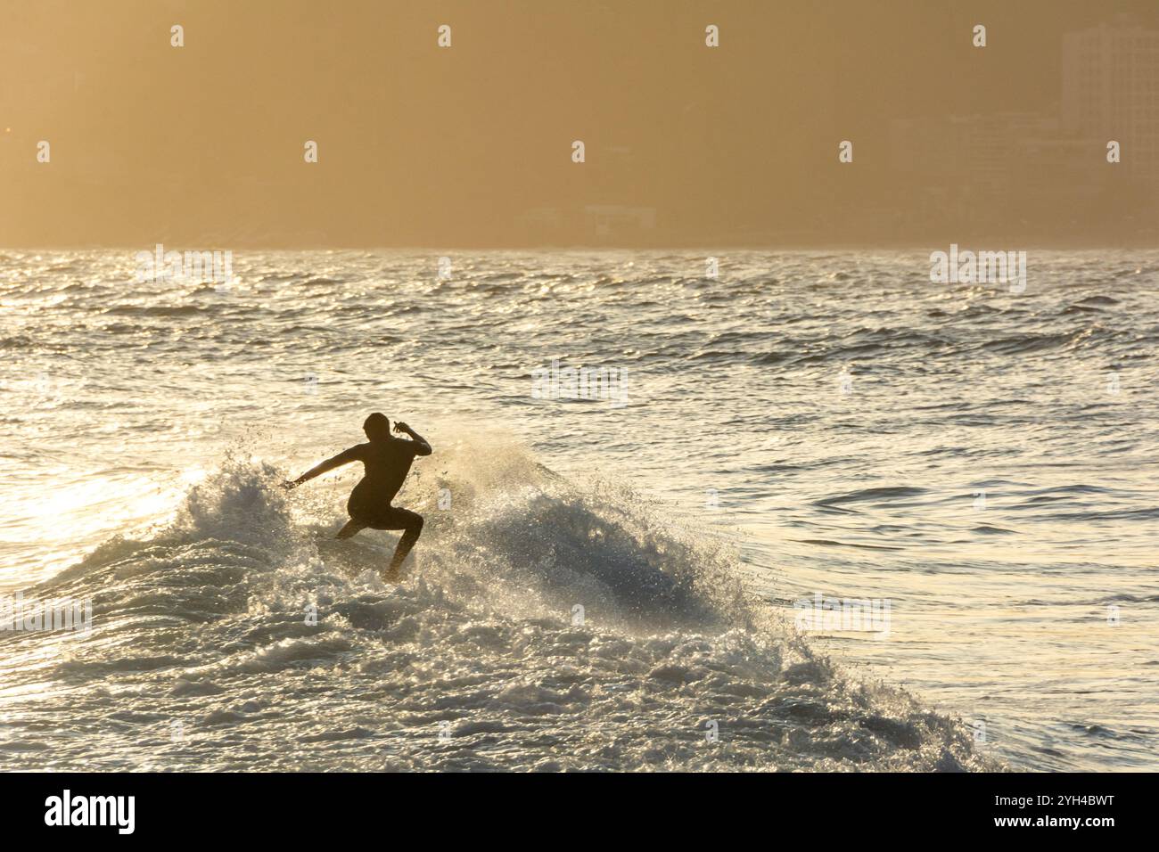 Surfista cavalcando le onde al tramonto alla spiaggia di Ipanema a Rio de Janeiro in Brasile Foto Stock
