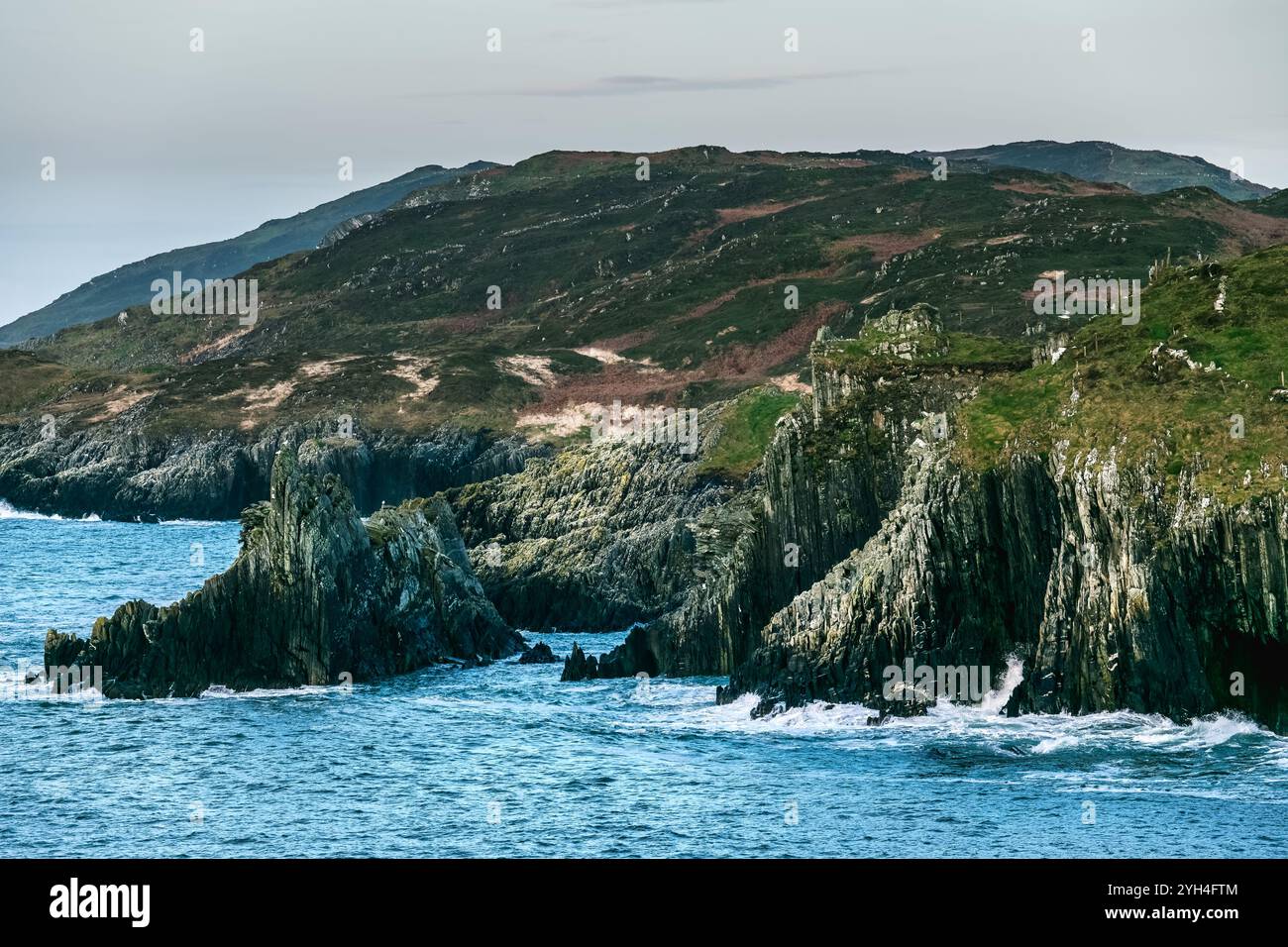 Scogliere costiere e acque tranquille vicino a un paesaggio aspro in Irlanda durante una giornata nuvolosa. Foto Stock