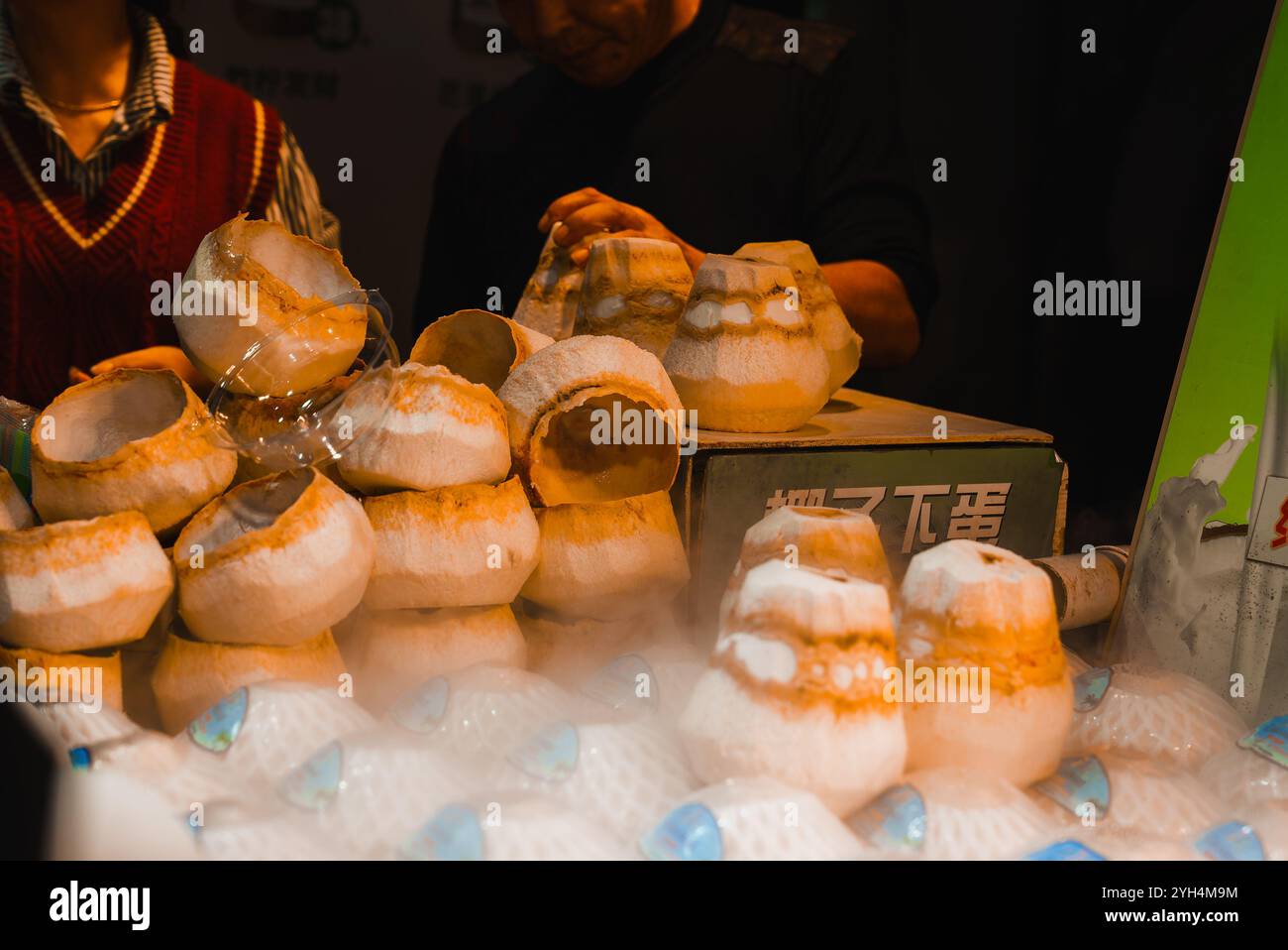 Uno stand di cibo di strada a Shanghai mostra noci di cocco con la parte superiore tagliata, rivelando carne bianca. La nebbia circonda le noci di cocco, aggiungendo un effetto visivo unico Foto Stock