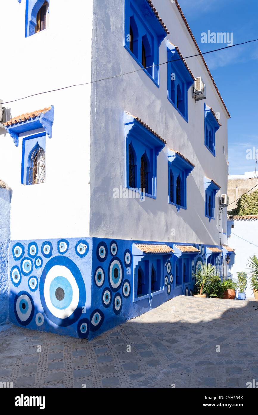 Un edificio dipinto di bianco con finestre di colore blu, parte del muro dipinta con cerchi blu nella medina di Chefchaouen, Marocco. Foto Stock