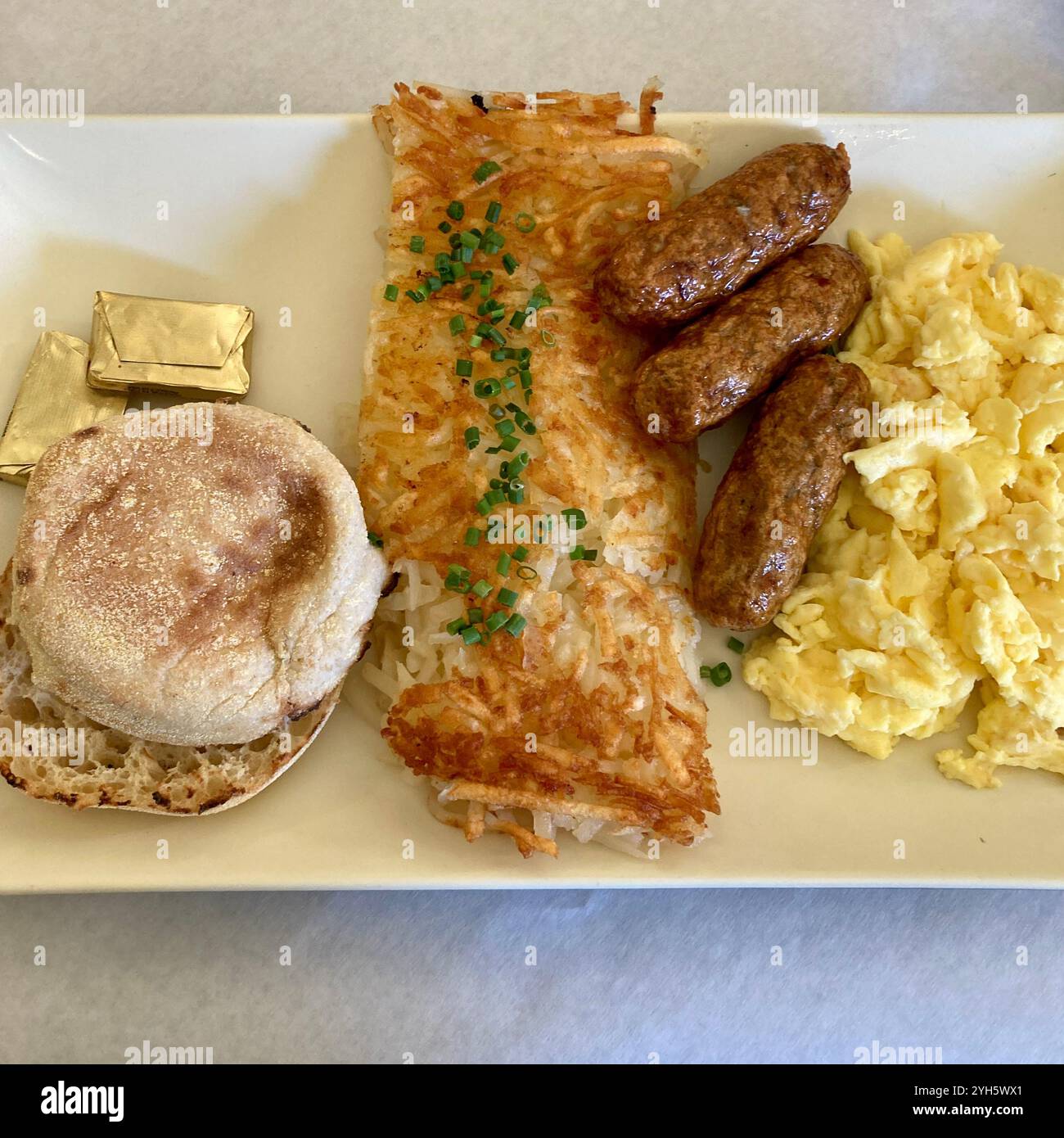Una colazione a base di crocchette di patate, salsicce, uova e un muffin inglese viene servita in un ristorante. Foto Stock