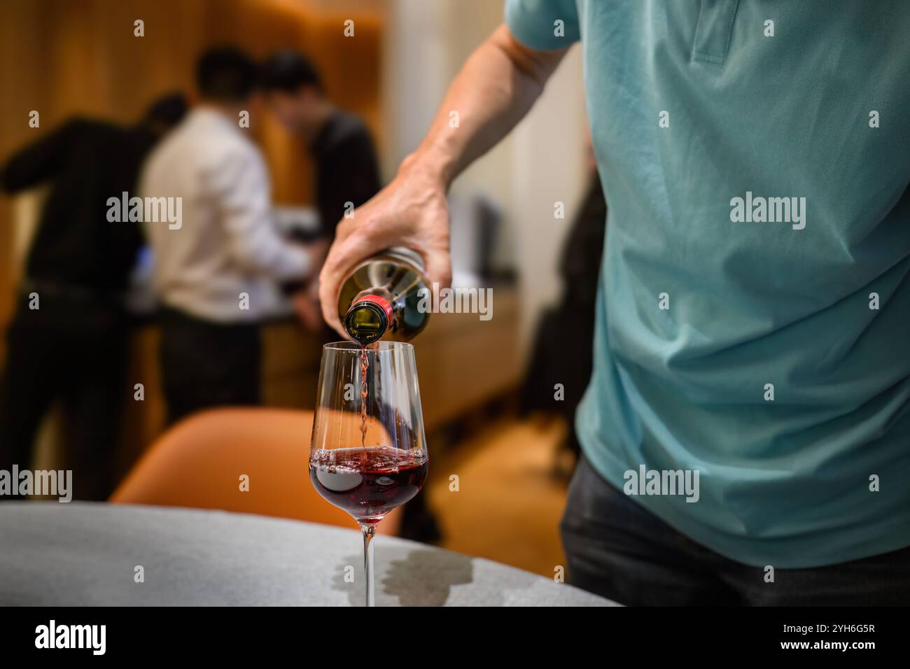 Uomo che versa vino rosso ai bicchieri di vino del ristorante. Personale irriconoscibile in background. Foto Stock