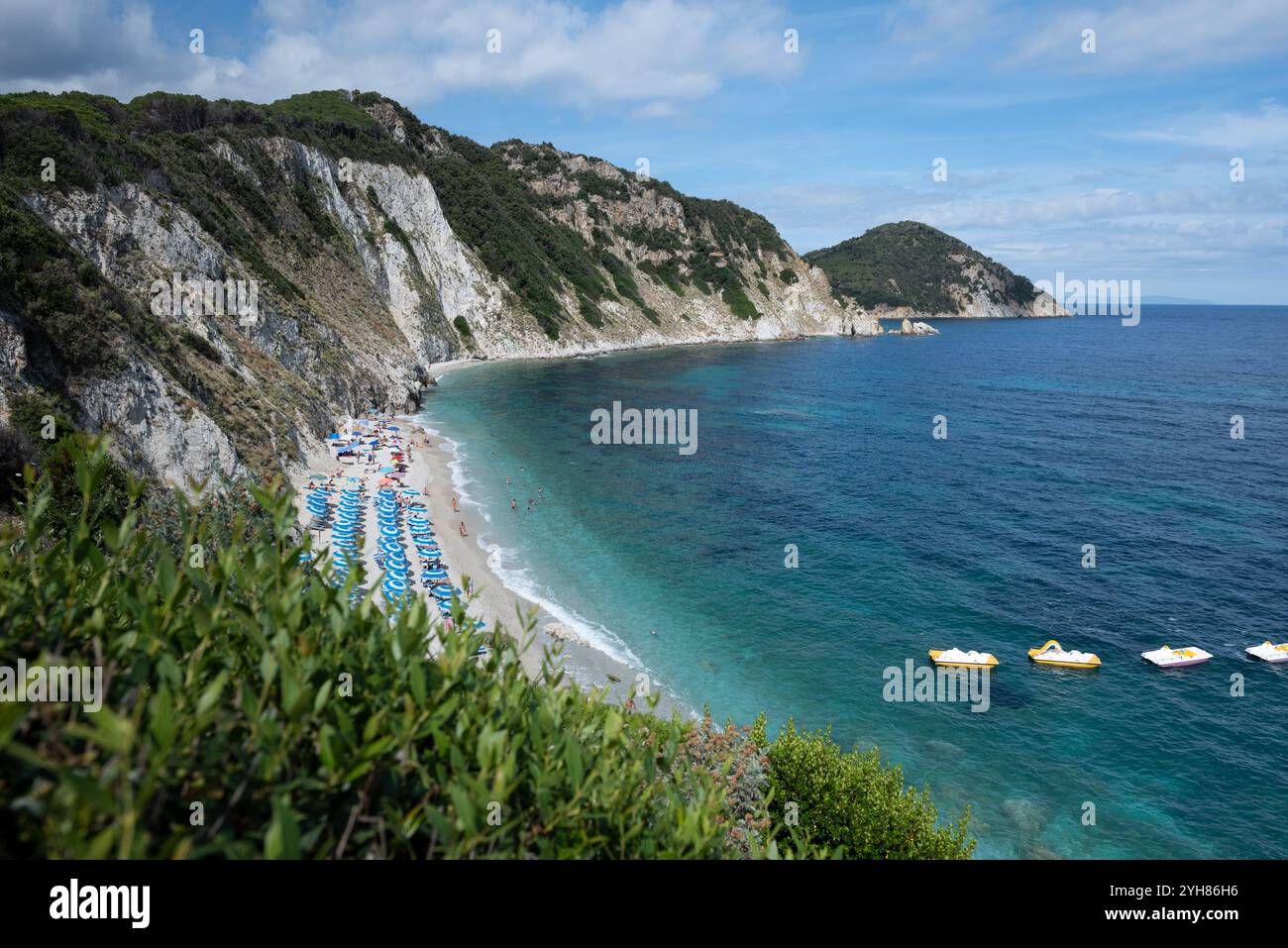 Spiaggia di Sansone all'Isola d'Elba in estate, con lettini e ombrellone con bagnanti in riva al mare e tavole da paddle gialle Foto Stock