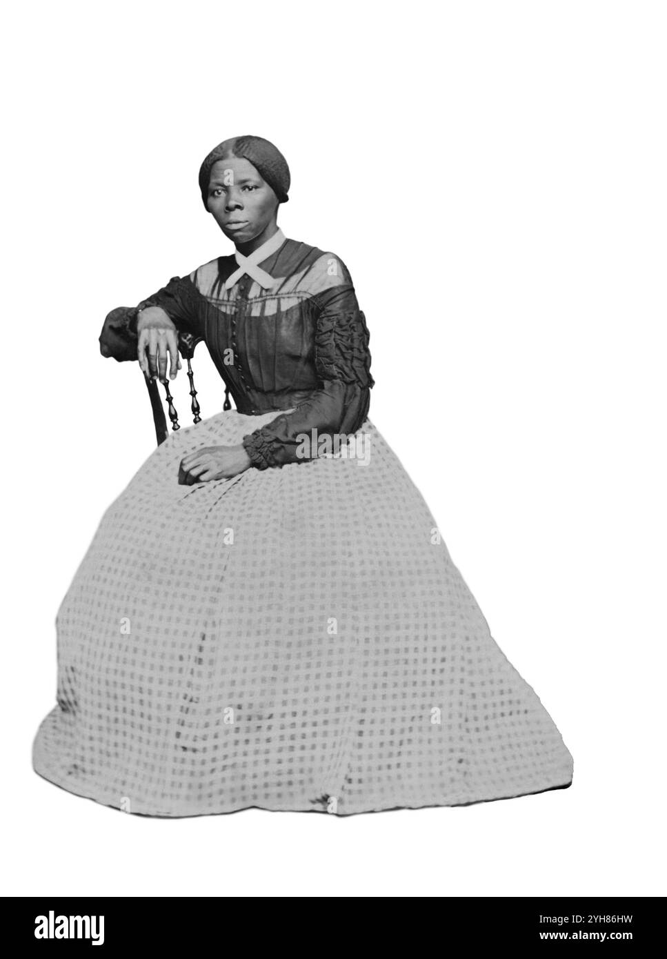 Una carta-de-visite di Harriet Tubman (circa 46-47) nel 1868-69. E' seduta, girata verso sinistra. Una mano poggia sul retro di una sedia di legno, un'altra sulle sue ginocchia. Creato da Benjamin Powelson, 77 Genesee St., Auburn, New York. Harriet Tubman seduto in una stanza interna. È posizionata leggermente girata a destra e guarda fuori dalla telecamera. La sua mano destra poggia sul retro di una sedia di legno e la sua mano sinistra è in grembo. Un tappeto dai motivi audaci copre il pavimento e la parete o la goccia dietro di lei è di colore chiaro vuoto. Tubman indossa un corpetto nero che si abbotta nella parte anteriore centrale e. Foto Stock