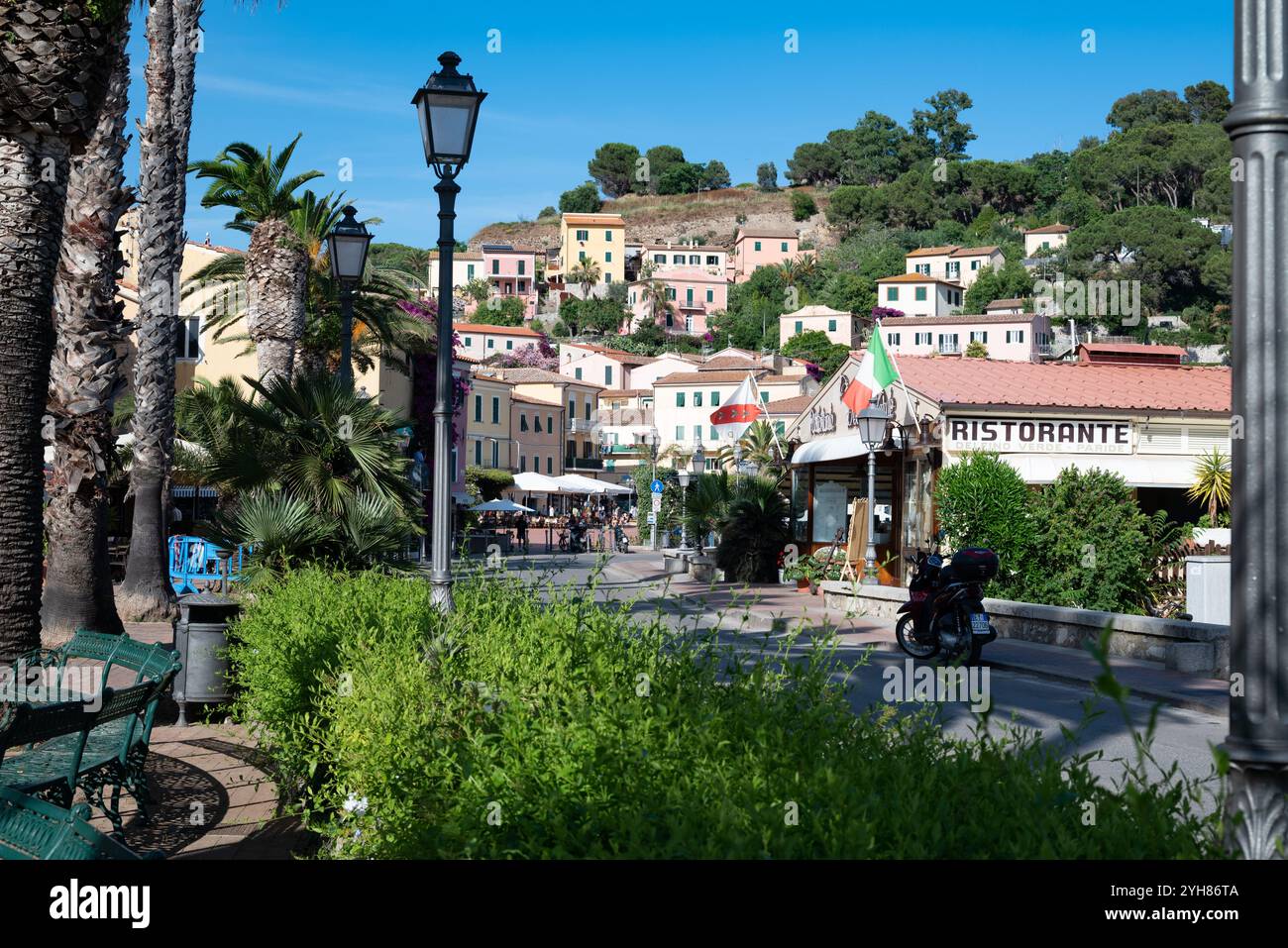 Una motocicletta parcheggiata fuori da un ristorante nel centro della città di Porto Azzurro all'Isola d'Elba in Toscana. Le case si trovano sul lato della collina Foto Stock