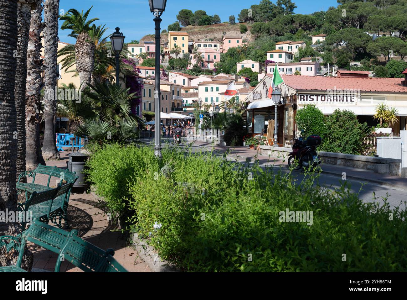 Una motocicletta parcheggiata fuori da un ristorante con bandiera italiana nel centro di Porto Azzurro all'Isola d'Elba in Toscana, la strada ha una vecchia c Foto Stock