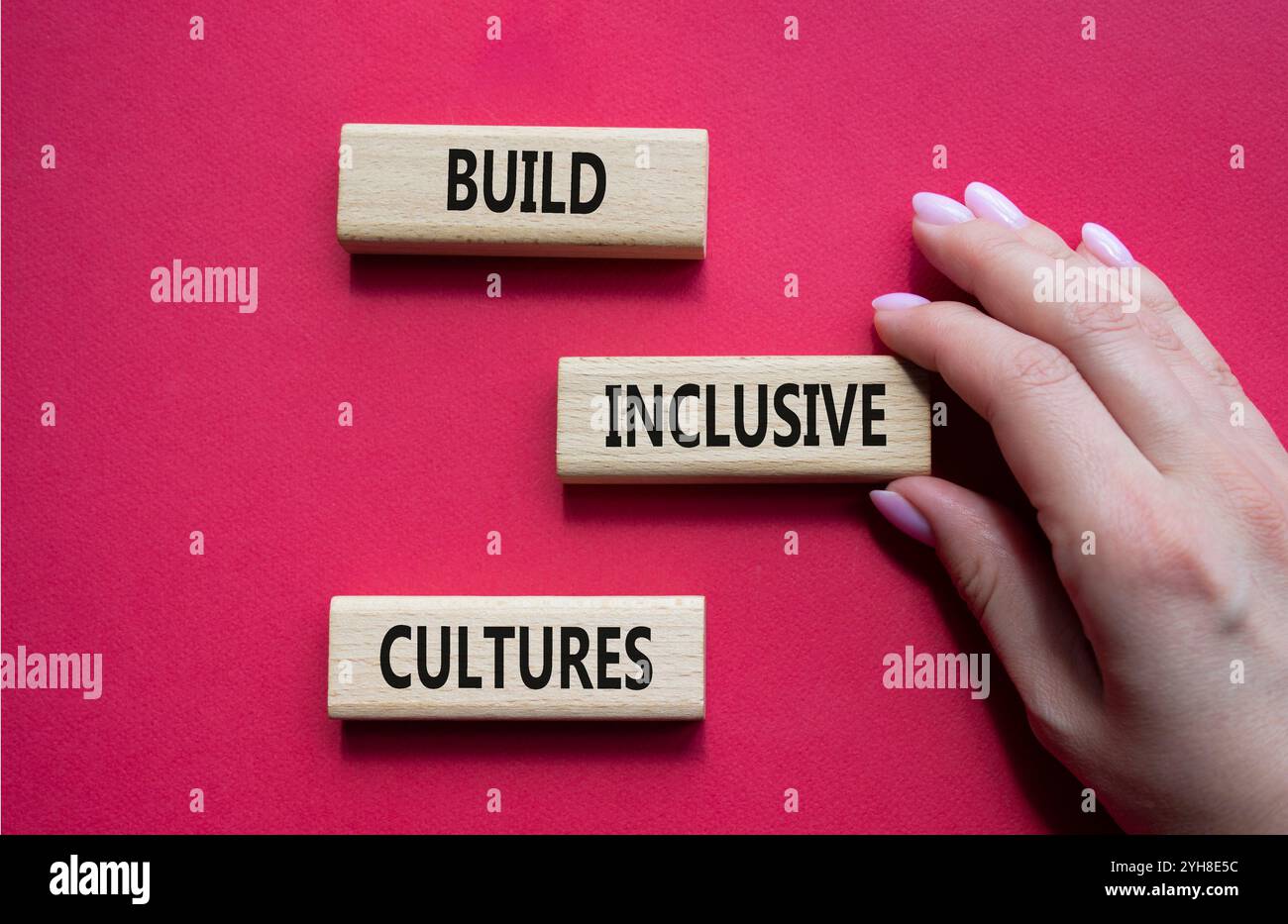 Simbolo di cultura inclusiva. Blocchi di legno con parole costruiscono culture inclusive. Bellissimo sfondo rosso. Mano d'affari. Business and Build Inc Foto Stock