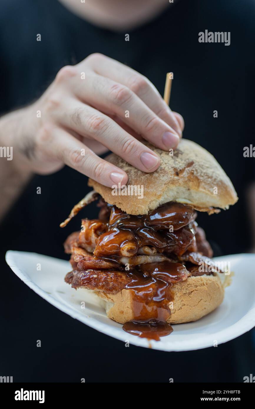 Primo piano di una persona con un'enorme salsiccia e bacon bap, un cibo tradizionale di Belfast, nell'Irlanda del Nord Foto Stock