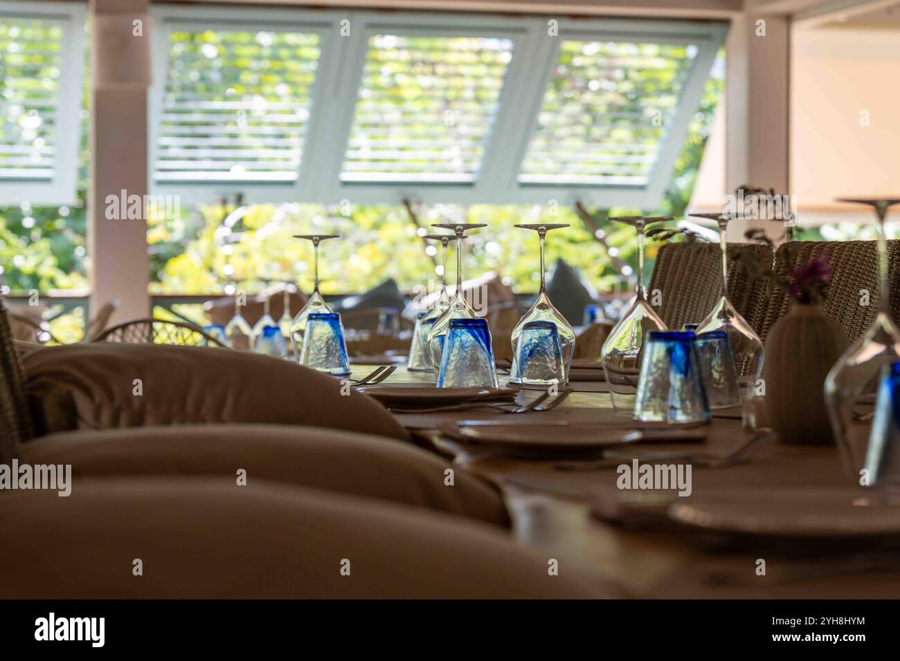 Bicchieri e posate su un tavolo del ristorante in un ambiente tropicale soleggiato con tende sullo sfondo Foto Stock