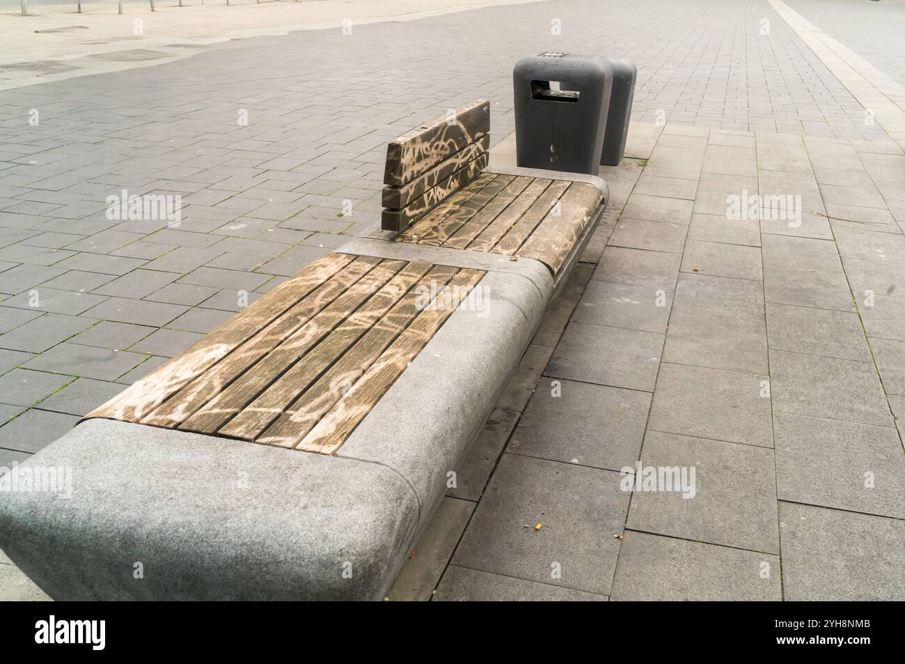 Bagnare la panchina in legno con graffiti vicino a due bidoni della spazzatura in una piazza deserta dopo la pioggia Foto Stock