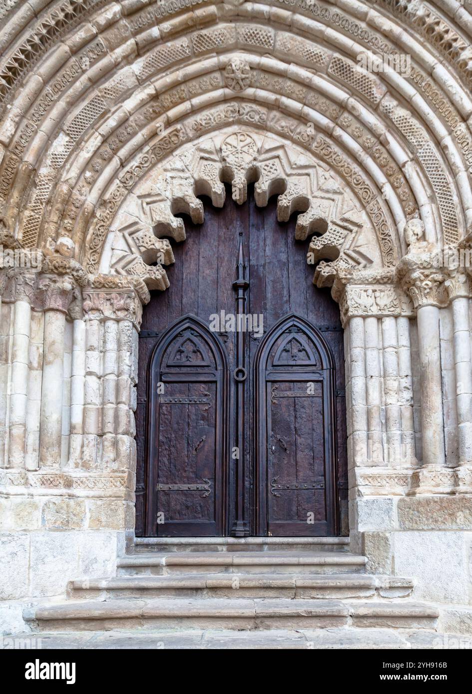 Un arco in pietra splendidamente intagliato incornicia le grandi porte in legno di un'antica chiesa di Estella, che mostra intricata maestria artigianale. Foto Stock