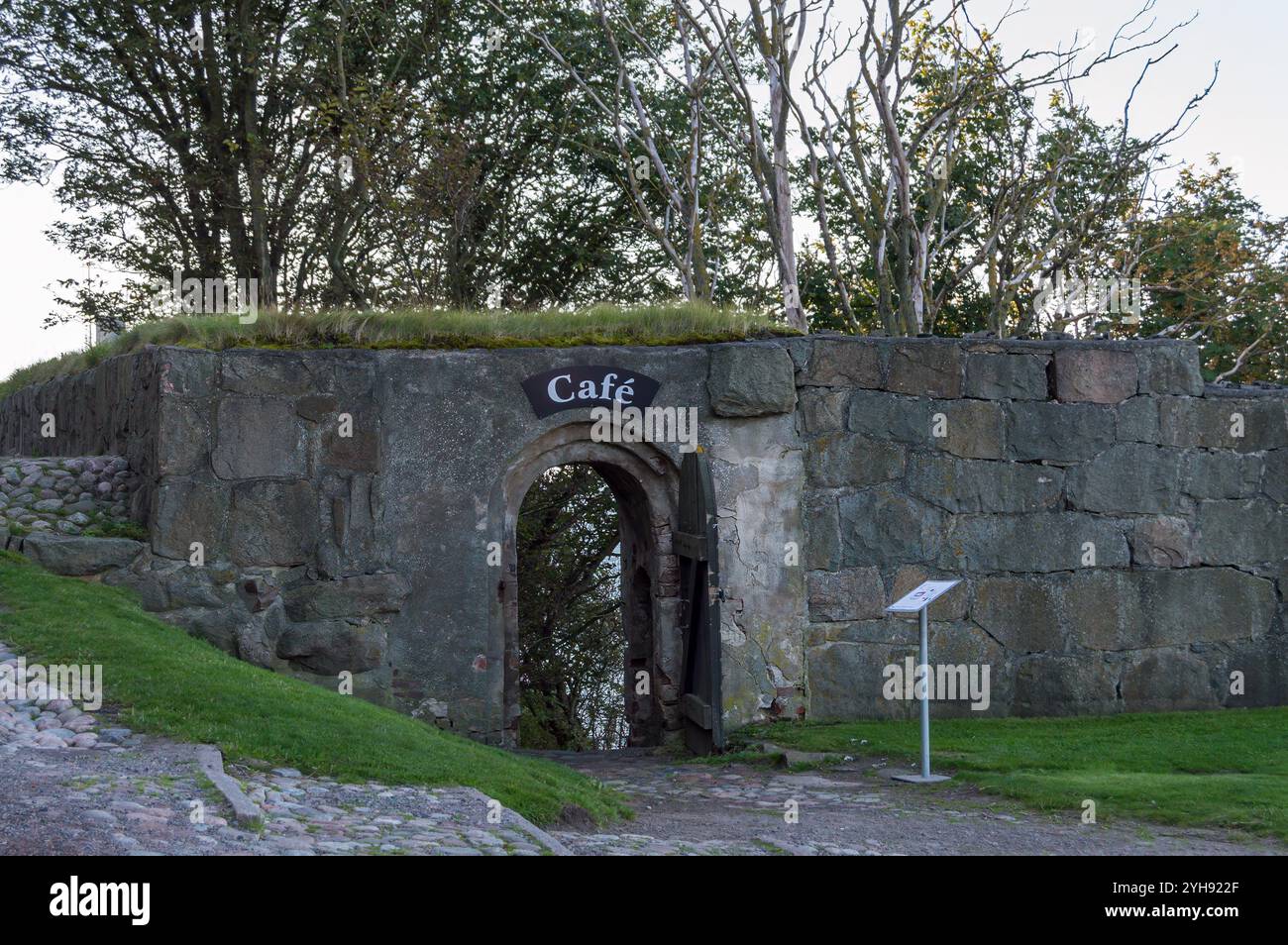 Un'affascinante arcata in pietra invita i visitatori in una pittoresca caffetteria, immersa nel verde. L'atmosfera rustica migliora l'esperienza di pace Foto Stock