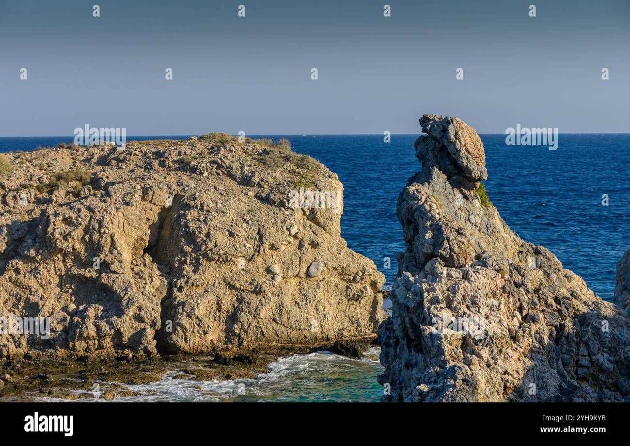 Le onde si infrangono dolcemente contro scogliere scoscese sotto un cielo azzurro, creando una tranquilla atmosfera costiera. Foto Stock