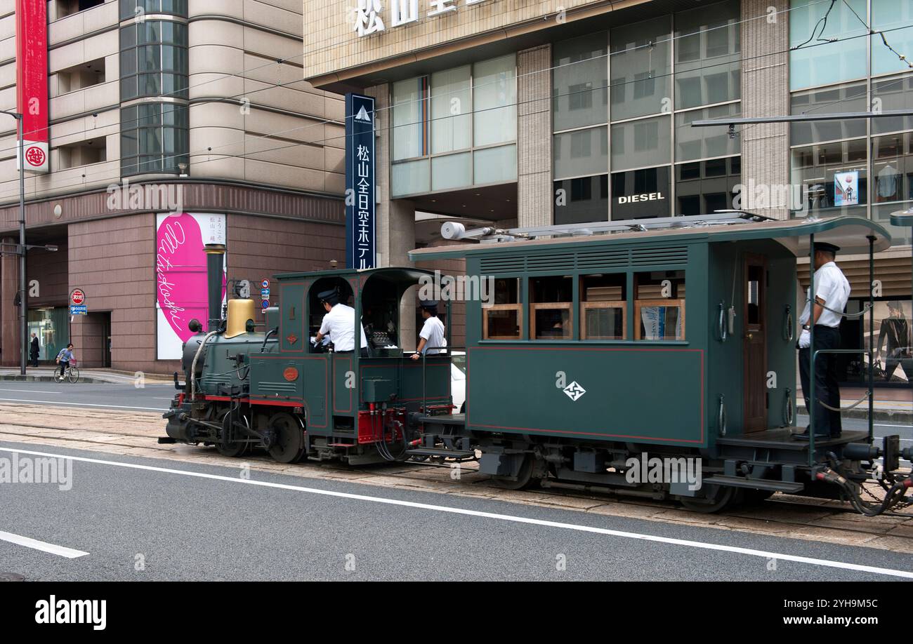 Il vecchio treno locomotivo Botchan Ressha che attraversa le strade di Matsuyama tra la stazione di Matsuyama e Dogo Onsen, Foto Stock