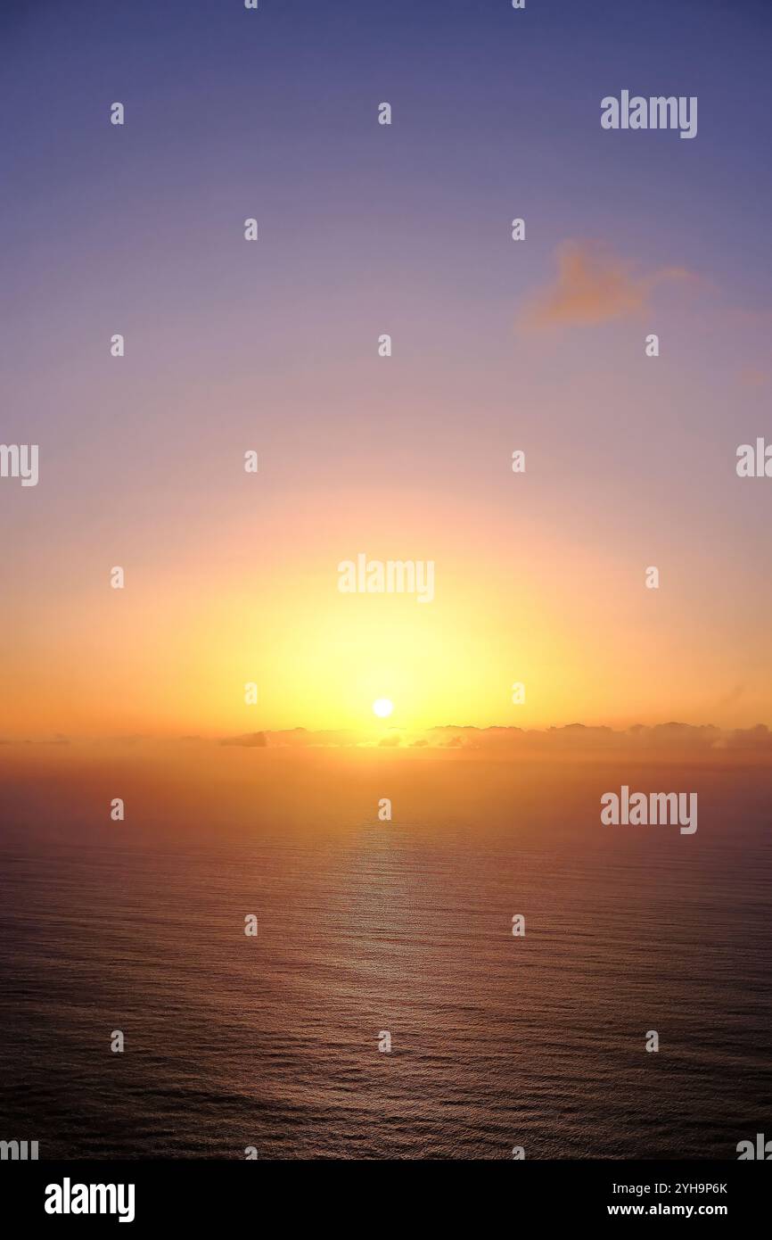 Un tranquillo paesaggio marino che cattura il tramonto sull'oceano. La luce soffusa del sole, appena sopra l'orizzonte, emette toni caldi sull'acqua. Foto Stock