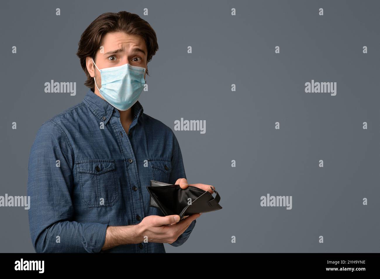 Coronavirus crisi economica. Worry Guy in Medical Mask (maschera medica) che mostra il portafoglio vuoto Foto Stock