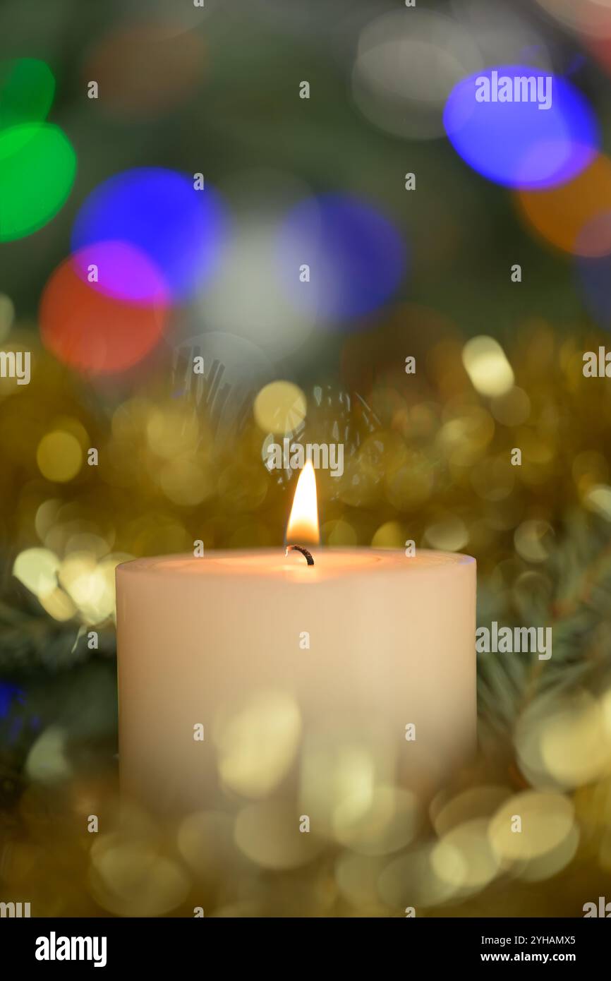 Candela bianca di Natale che brucia tranquillamente, con colorate luci bokeh intorno ad essa Foto Stock